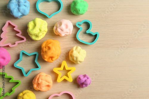 Different color play dough with molds on wooden table, flat lay. Space for text