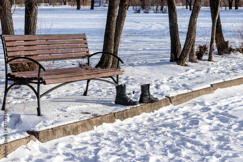 Winter black men's boots near a bench in an empty park