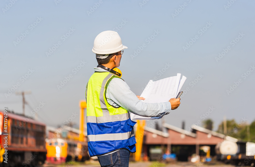 Engineer under inspection and checking construction process railway locomotive repair plant, Engineer man in waistcoats and hardhats and with documents in a railway depot Engineer under inspection and checking construction process railway locomotive repair plant, Engineer man in waistcoats and hardhats and with documents in a railway depot