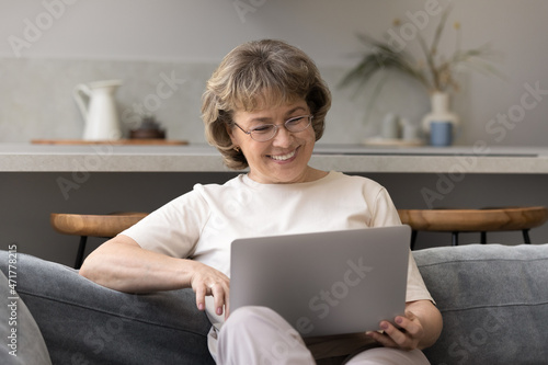 Happy mature 60s woman consulting doctor online, using online telehealth app on laptop, talking on video call, smiling. Older lady chatting on internet, watching funny movie, relaxing on sofa photo