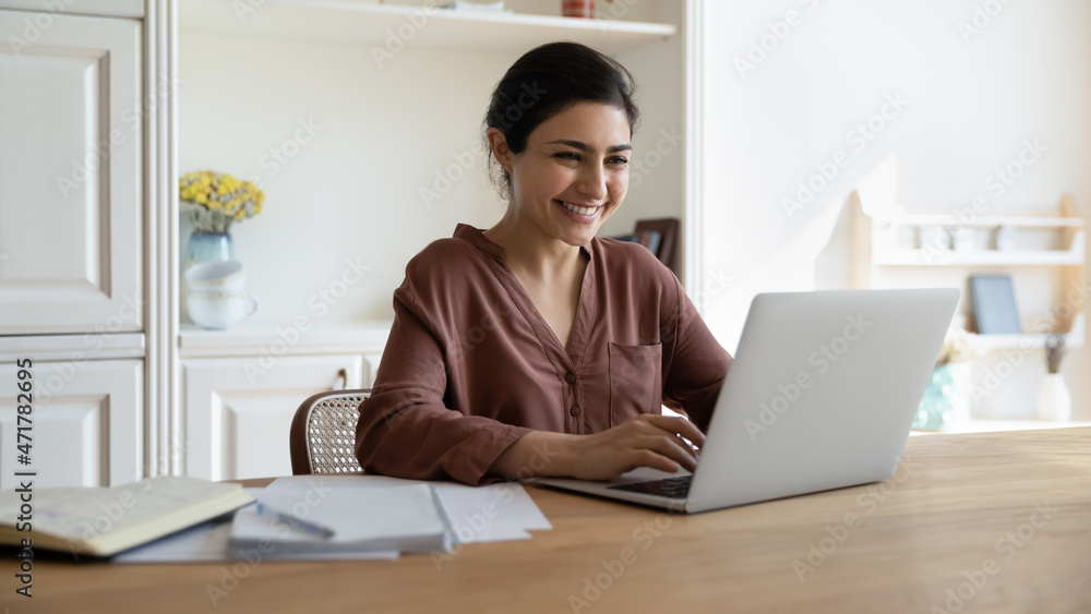 Happy millennial indian businesswoman working on computer in modern home office, checking email, communicating distantly. Smiling young female student studying on online courses, preparing for exams. Happy millennial indian businesswoman working on computer in modern home office, checking email, communicating distantly. Smiling young female student studying on online courses, preparing for exams.