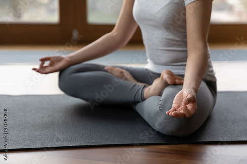 Close up mindful young indian woman in sportswear sitting in lotus pose on mat with folded in mudra gesture hands, involved in deep meditation, relaxing after yoga training, doing breathing exercises.