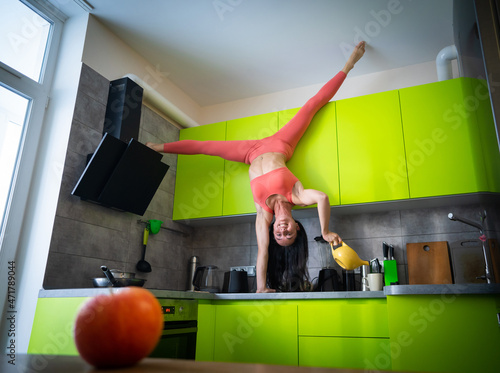 Fototapeta Flexible woman cooking upside down in kitchen