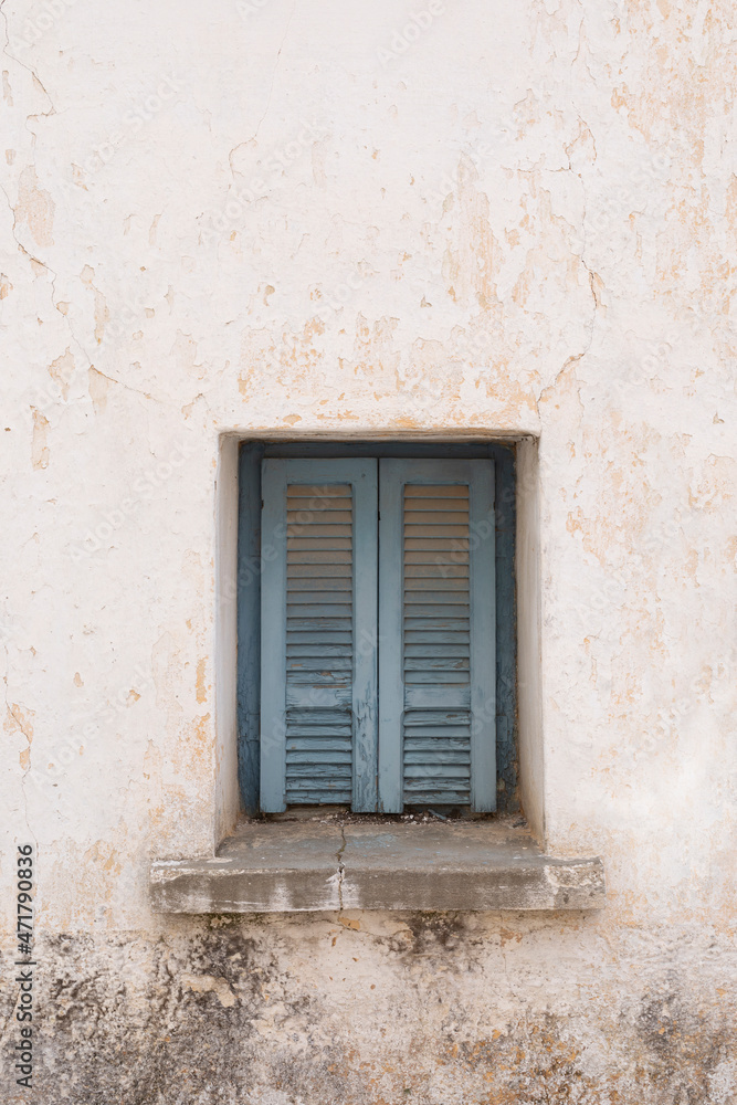 White wall with blue old wooden window with closed shutters, Stone wall with rough and cracked surface, vertical format
