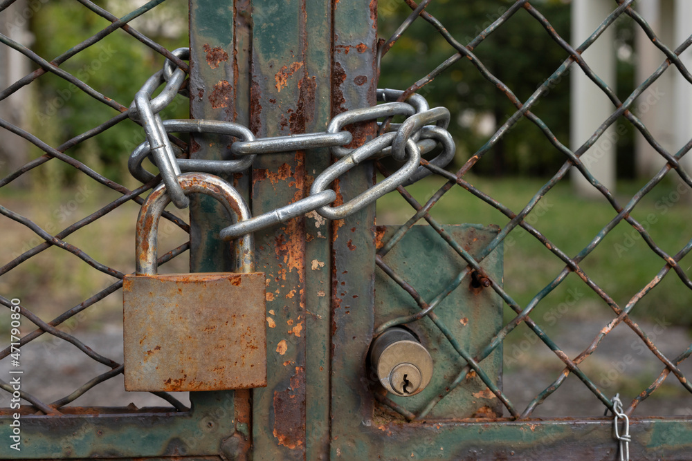 Lock down, old rusty padlock on a mesh fence with metal chain, safety first, no person Lock down, old rusty padlock on a mesh fence with metal chain, safety first, no person