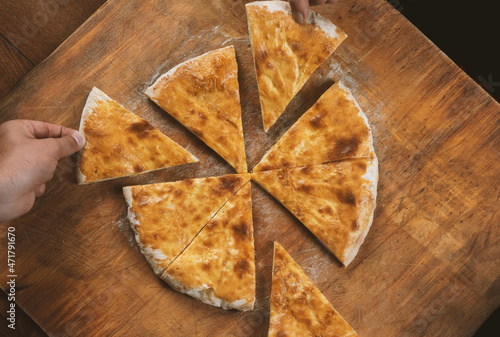 Persons take pieces of baked homemade cheese pie on wooden background. Bulgarian banitsa, Georgian khachapuri, Greek tiropita photo