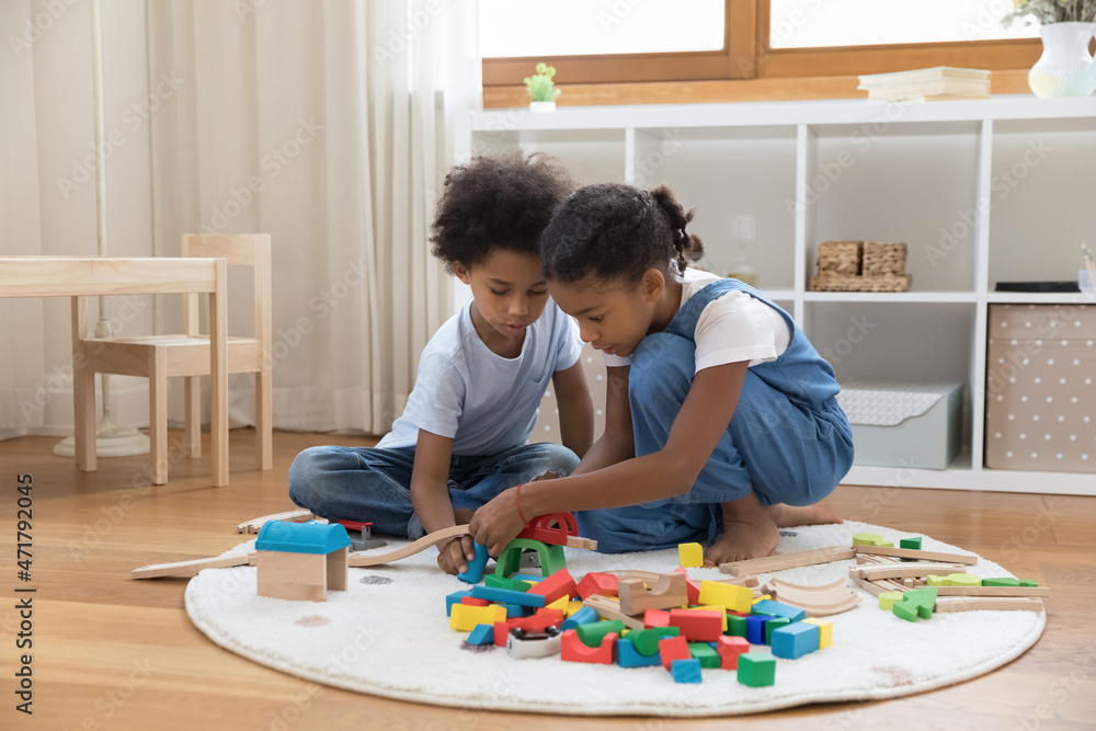Two mixed race sibling kids playing with heap of colorful toys on heating floor at home. Little brother and sister completing construction model, building road, railway, improving skills in game Two mixed race sibling kids playing with heap of colorful toys on heating floor at home. Little brother and sister completing construction model, building road, railway, improving skills in game