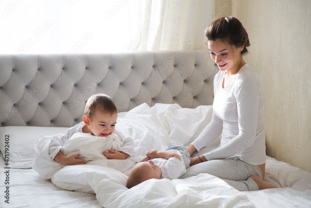 mother hugs and plays with two little kids lying in bed in the morning. mother spends time with two young children at home mother hugs and plays with two little kids lying in bed in the morning. mother spends time with two young children at home