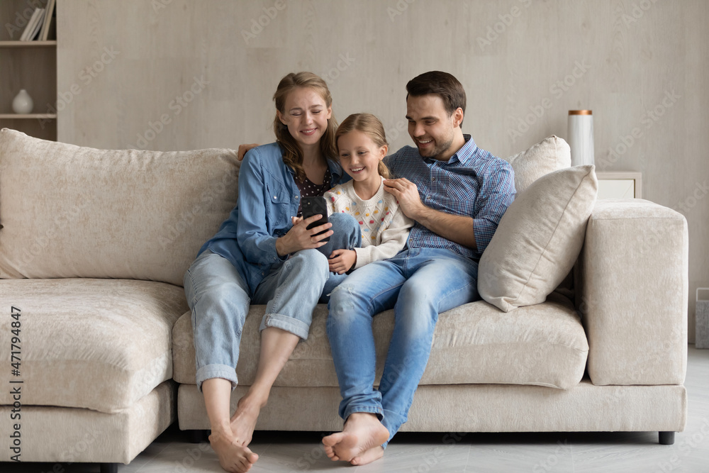 Full length bonding Caucasian two generations family using smartphone, resting on cozy sofa in modern living room. Addicted to modern tech happy young couple parents and little daughter playing games. Full length bonding Caucasian two generations family using smartphone, resting on cozy sofa in modern living room. Addicted to modern tech happy young couple parents and little daughter playing games.