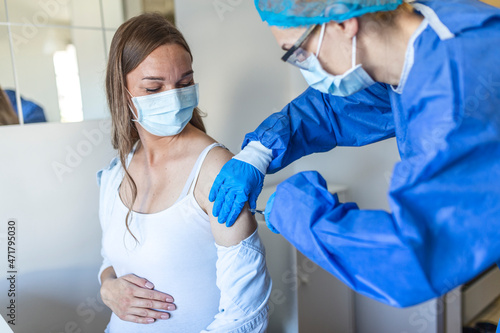 Female doctor giving Covid-19 vaccine injection to young pregnant woman at health centre. Expectant lady being immunized against coronavirus at clinic. Population vaccination concept photo