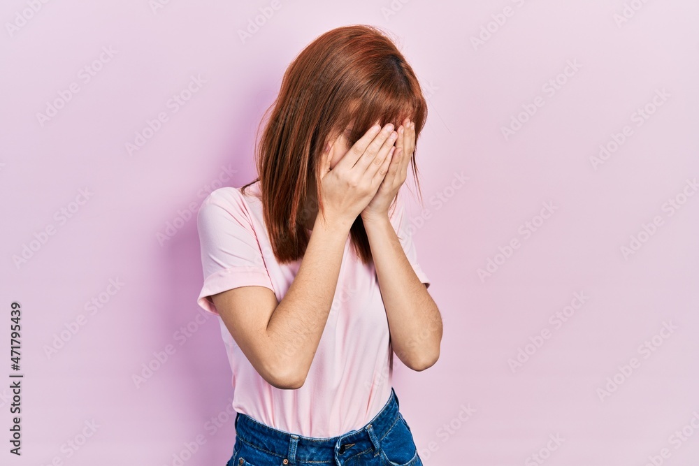 Redhead young woman wearing casual pink t shirt with sad expression covering face with hands while crying. depression concept. Redhead young woman wearing casual pink t shirt with sad expression covering face with hands while crying. depression concept.