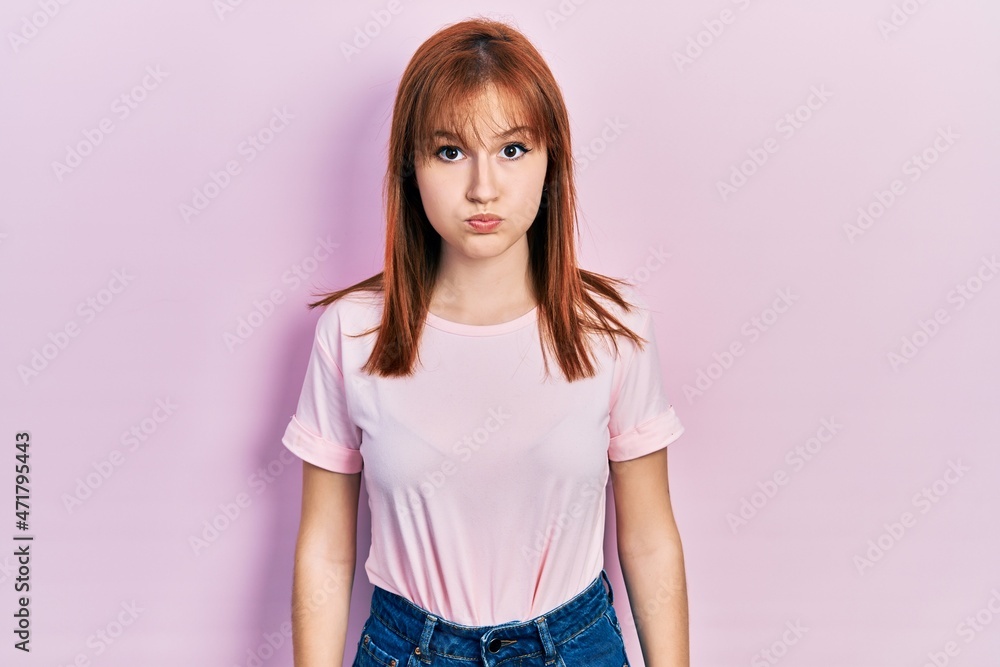 Redhead young woman wearing casual pink t shirt puffing cheeks with funny face. mouth inflated with air, crazy expression. Redhead young woman wearing casual pink t shirt puffing cheeks with funny face. mouth inflated with air, crazy expression.