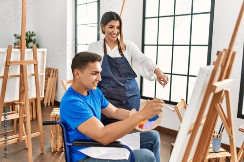 Teacher and disabled paint student sitting on wheelchair smiling happy painting at art school.