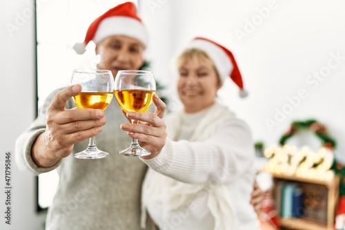 Middle age caucasian couple wearing christmas hat toasting with champagne at home.