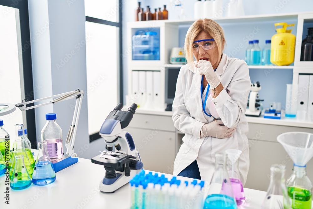 Middle age blonde woman working at scientist laboratory feeling unwell and coughing as symptom for cold or bronchitis. health care concept. Middle age blonde woman working at scientist laboratory feeling unwell and coughing as symptom for cold or bronchitis. health care concept.
