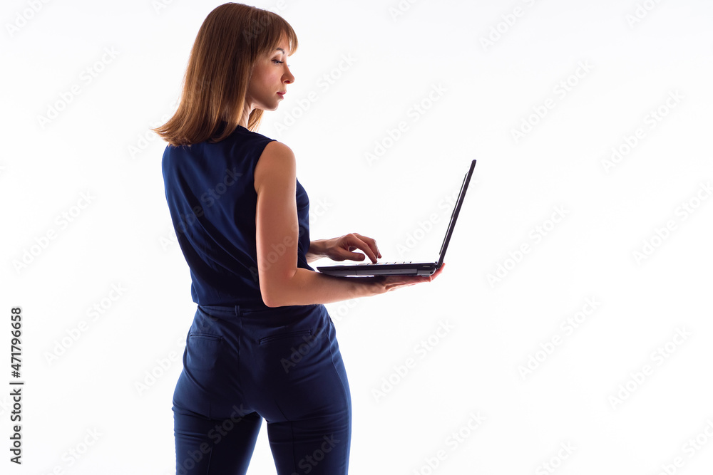Woman with laptop over white background. Businesswoman in blue clothes. She is standing with her back to camera and is typing something. Businesswoman with computer. Portrait of businesswoman.