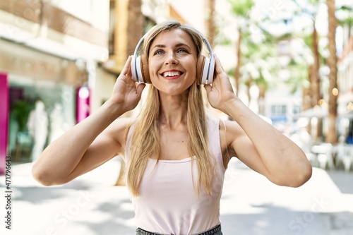 Beautiful blonde woman smiling happy outdoors on a sunny day wearing headphones listening to music © Krakenimages.com