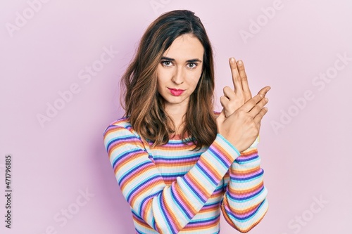 Young hispanic girl wearing casual clothes holding symbolic gun with hand gesture, playing killing shooting weapons, angry face