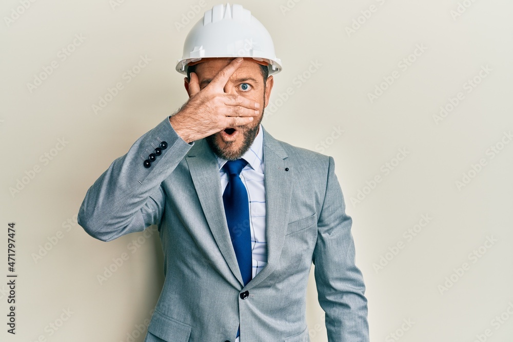 Middle age man wearing architect hardhat peeking in shock covering face and eyes with hand, looking through fingers afraid Middle age man wearing architect hardhat peeking in shock covering face and eyes with hand, looking through fingers afraid