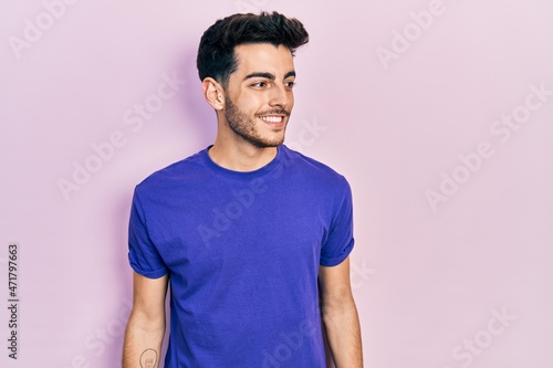 Young hispanic man wearing casual t shirt looking away to side with smile on face, natural expression. laughing confident.