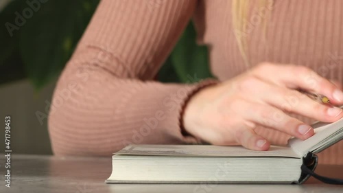 Close-up of woman's hands finishing writing an idea in notebook with a pen, putting a ribbon book maker and closing it