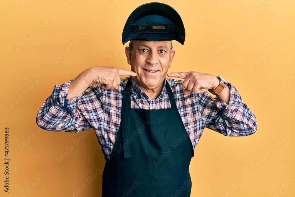 Fototapeta premium Handsome senior man with grey hair wearing welding protection mask smiling cheerful showing and pointing with fingers teeth and mouth. dental health concept.