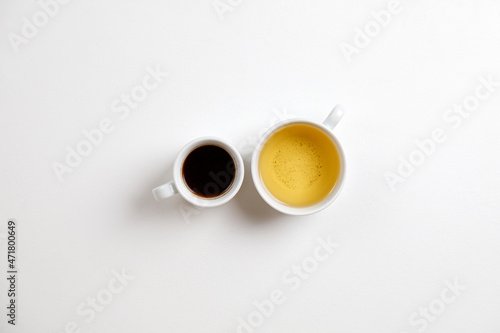 Coffee opposite tea. Mug of black coffee opposite mug of green tea on a white table. Minimalism.
