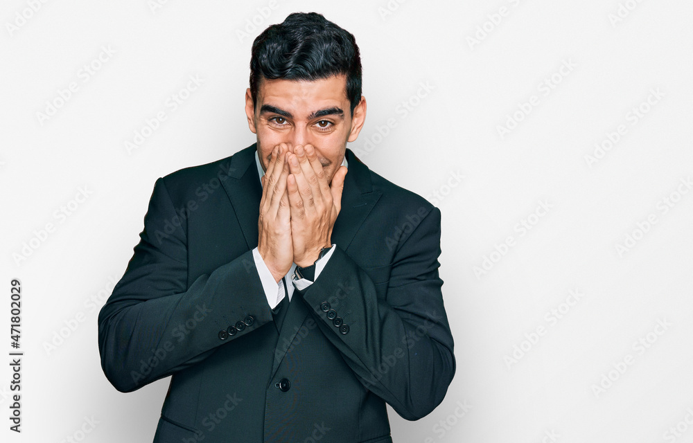 Handsome hispanic man wearing business clothes laughing and embarrassed giggle covering mouth with hands, gossip and scandal concept Handsome hispanic man wearing business clothes laughing and embarrassed giggle covering mouth with hands, gossip and scandal concept