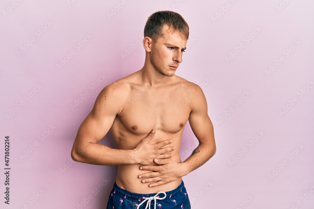 Fototapeta premium Young caucasian man wearing swimwear with hand on stomach because indigestion, painful illness feeling unwell. ache concept.