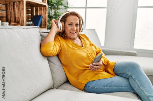 Middle age caucasian woman listening to music sitting on the sofa at home.