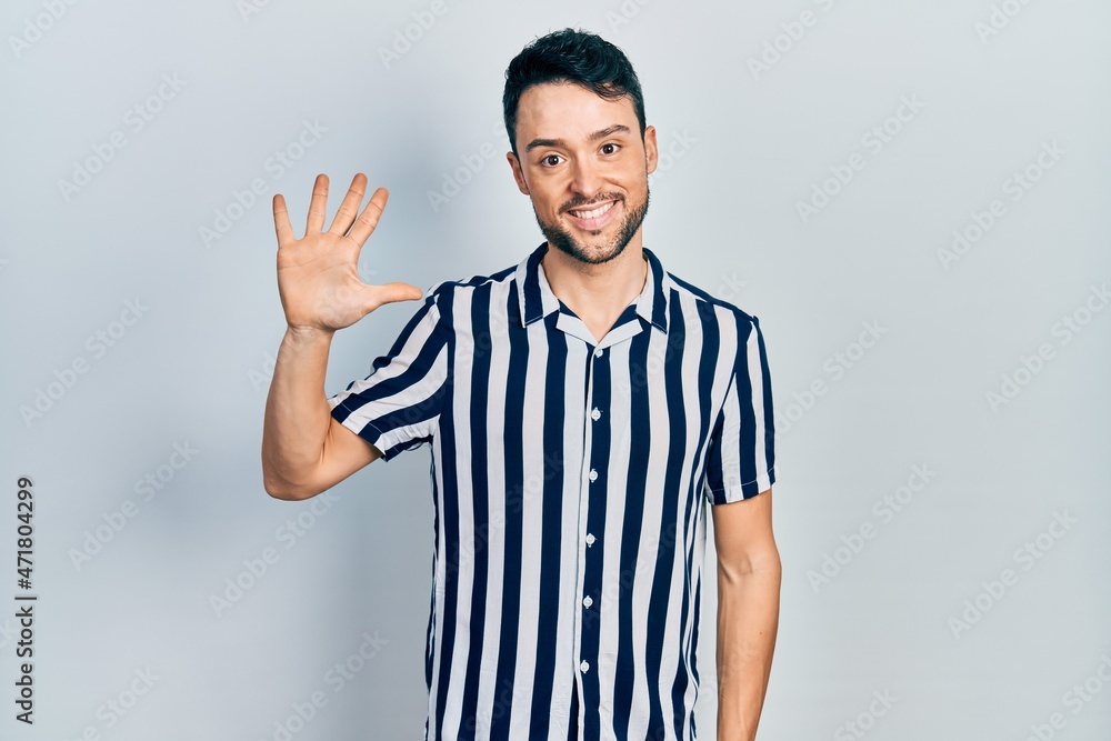 Fototapeta premium Young hispanic man wearing casual clothes showing and pointing up with fingers number five while smiling confident and happy.