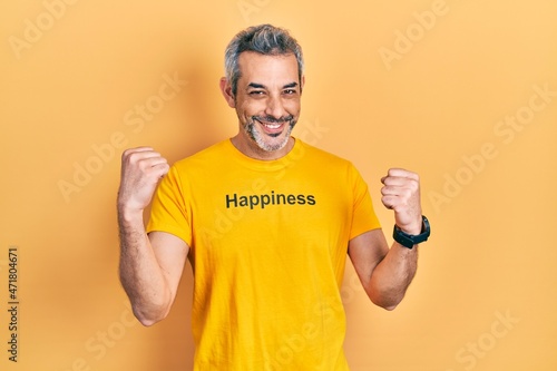 Handsome middle age man with grey hair wearing t shirt with happiness word message screaming proud, celebrating victory and success very excited with raised arms