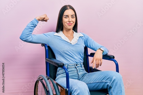 Beautiful woman with blue eyes sitting on wheelchair strong person showing arm muscle, confident and proud of power