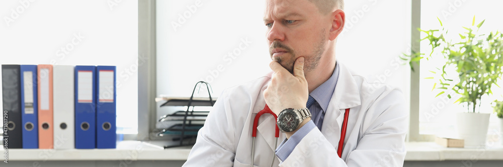 Pensive doctor looking at laptop screen and typing on keyboard in clinic Pensive doctor looking at laptop screen and typing on keyboard in clinic