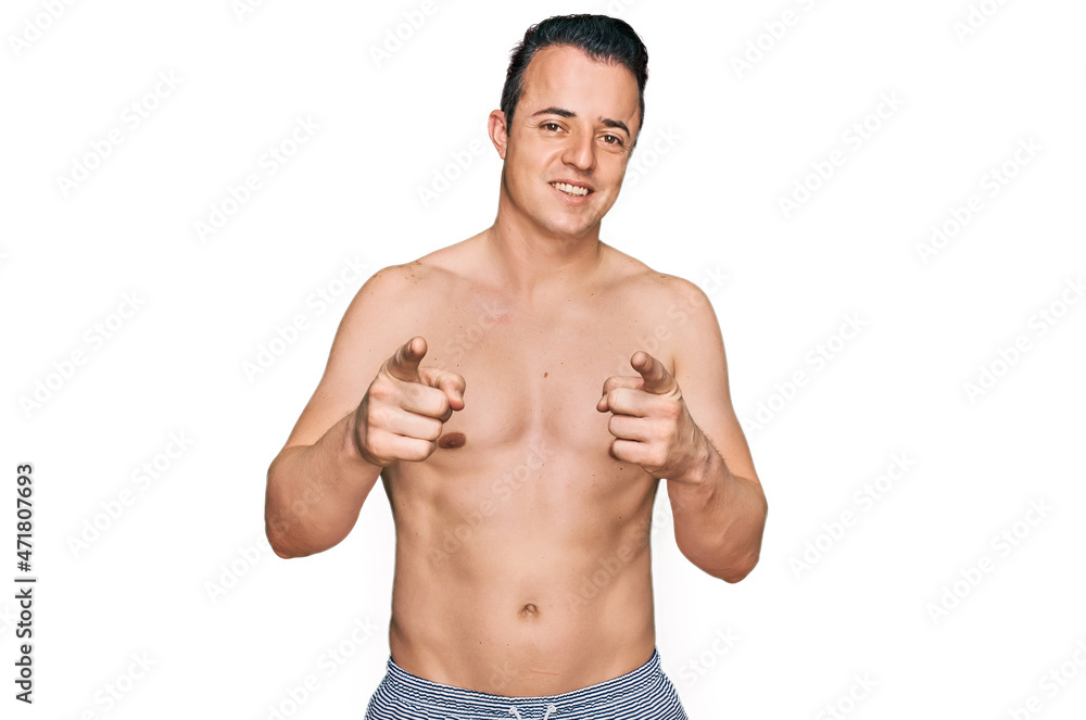 Handsome young man wearing swimwear shirtless pointing fingers to camera with happy and funny face. good energy and vibes.