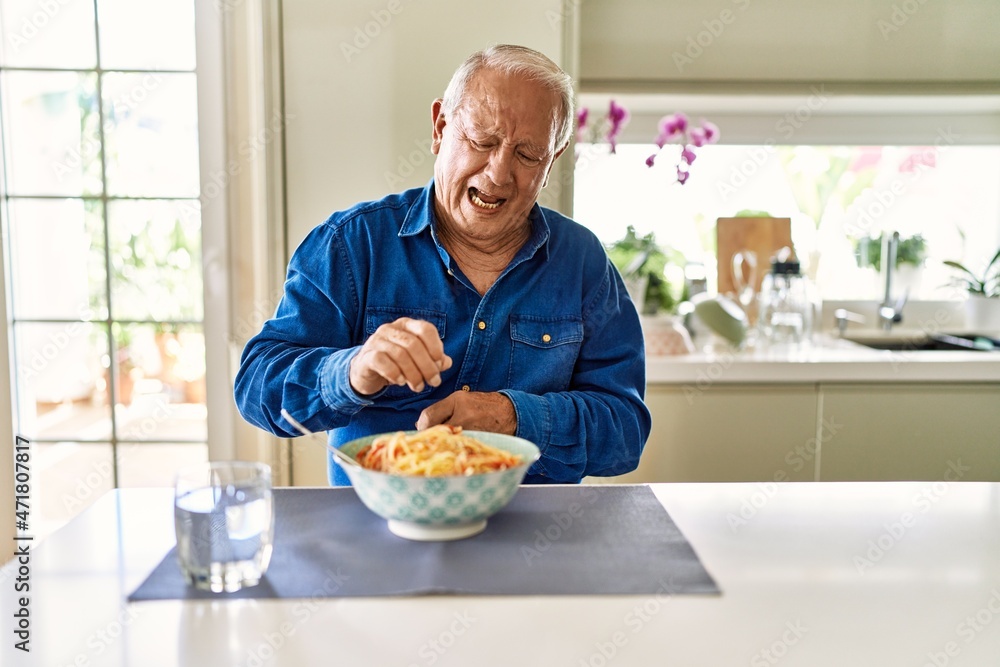 Senior man with grey hair eating pasta spaghetti at home disgusted expression, displeased and fearful doing disgust face because aversion reaction. with hands raised Senior man with grey hair eating pasta spaghetti at home disgusted expression, displeased and fearful doing disgust face because aversion reaction. with hands raised
