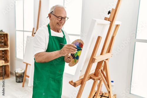 Senior grey-haired artist man smiling happy painting at art studio.