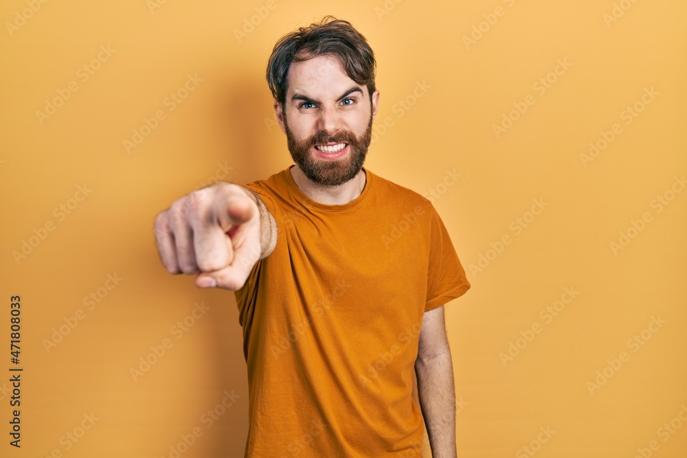 Caucasian man with beard wearing casual yellow t shirt pointing displeased and frustrated to the camera, angry and furious with you Caucasian man with beard wearing casual yellow t shirt pointing displeased and frustrated to the camera, angry and furious with you