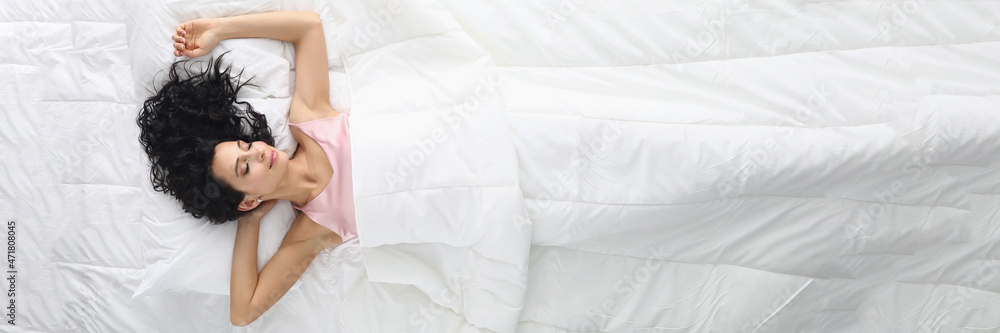 Young woman with curly hair sleeping in white bed top view Young woman with curly hair sleeping in white bed top view