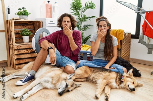 Canvas Print Young hispanic couple doing laundry with dogs bored yawning tired covering mouth with hand