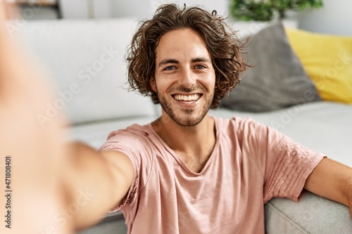 Young hispanic man smiling happy make selfie by the camera sitting on the floor at home. © Krakenimages.com