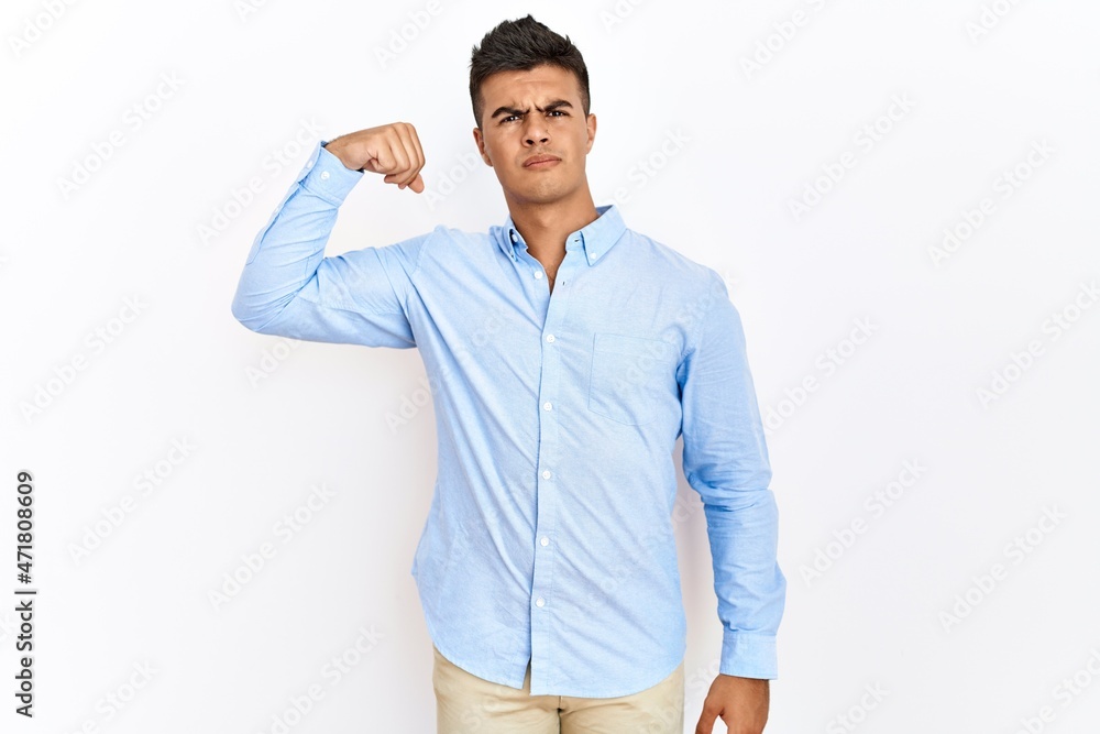 Young hispanic man wearing business shirt standing over isolated background strong person showing arm muscle, confident and proud of power Young hispanic man wearing business shirt standing over isolated background strong person showing arm muscle, confident and proud of power