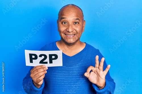 Middle age latin man holding p2p message paper doing ok sign with fingers, smiling friendly gesturing excellent symbol