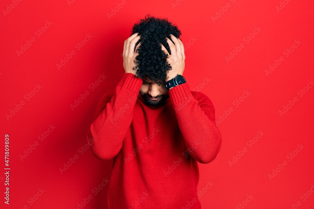 Young arab man with beard wearing casual red sweater suffering from headache desperate and stressed because pain and migraine. hands on head. Young arab man with beard wearing casual red sweater suffering from headache desperate and stressed because pain and migraine. hands on head.