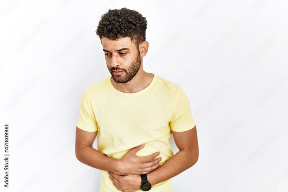Arab young man standing over isolated background with hand on stomach because indigestion, painful illness feeling unwell. ache concept. Arab young man standing over isolated background with hand on stomach because indigestion, painful illness feeling unwell. ache concept.