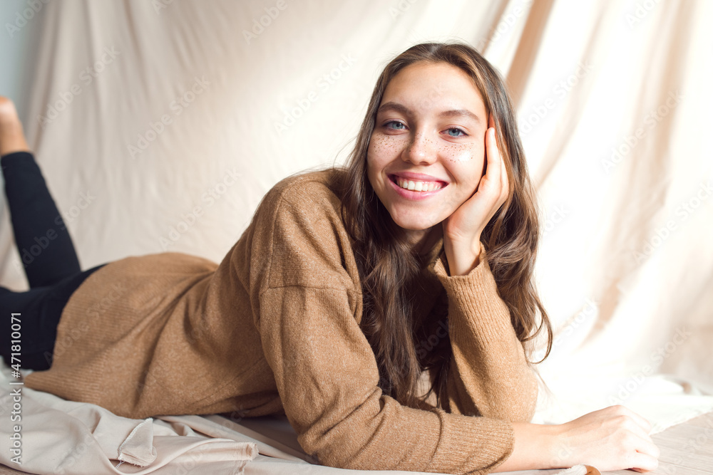 beautiful teenage girl with golden freckles on face posing on beige background, laying on floor beautiful teenage girl with golden freckles on face posing on beige background, laying on floor