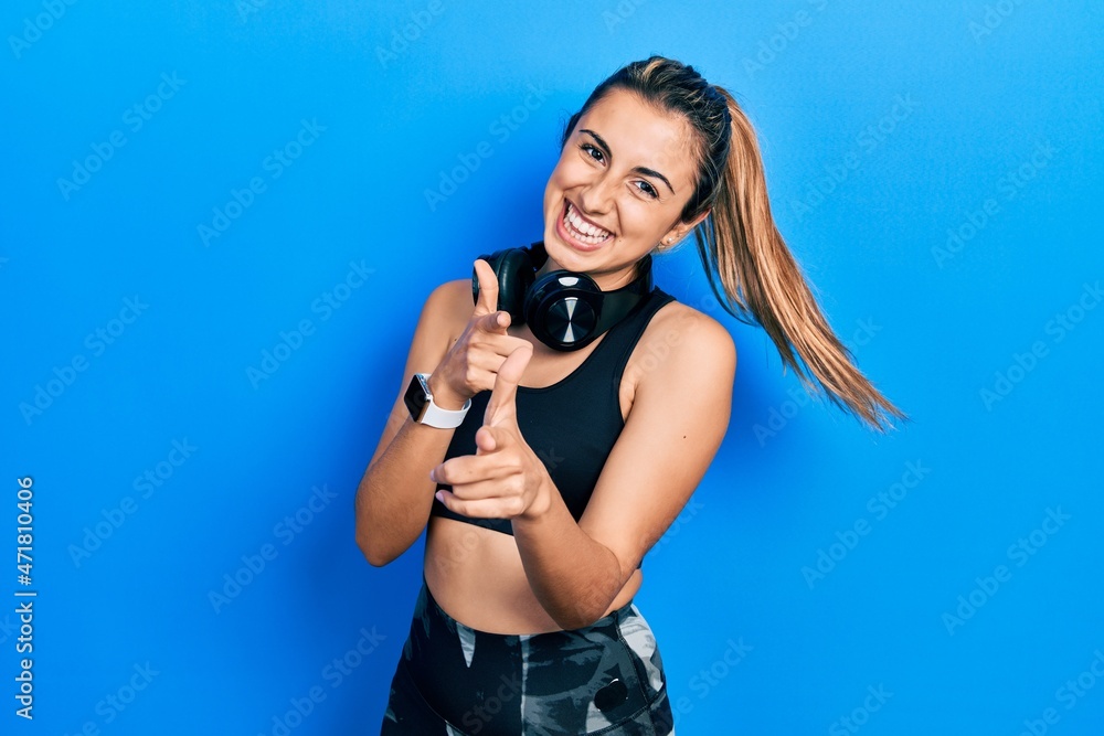 Beautiful hispanic woman wearing gym clothes and using headphones pointing fingers to camera with happy and funny face. good energy and vibes. Beautiful hispanic woman wearing gym clothes and using headphones pointing fingers to camera with happy and funny face. good energy and vibes.