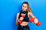 Beautiful hispanic woman wearing sportswear using dumbbells skeptic and nervous, frowning upset because of problem. negative person.