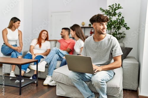 Group of young friends speaking sitting on the sofa. Man smilimg happy and using laptop at home.