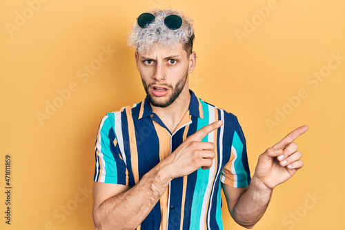 Young hispanic man with modern dyed hair pointing with fingers to the side clueless and confused expression. doubt concept.